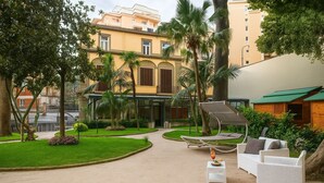 Un patio con zona de estar, palmeras y un edificio con balcones.