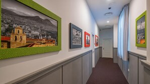 Un pasillo con obras de arte enmarcadas en las paredes, una alfombra estampada y una puerta al final.