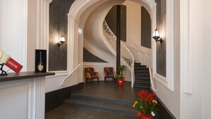 Una gran escalera con barandillas blancas y piso oscuro, que conduce a una zona de descanso con asientos y una planta en maceta.