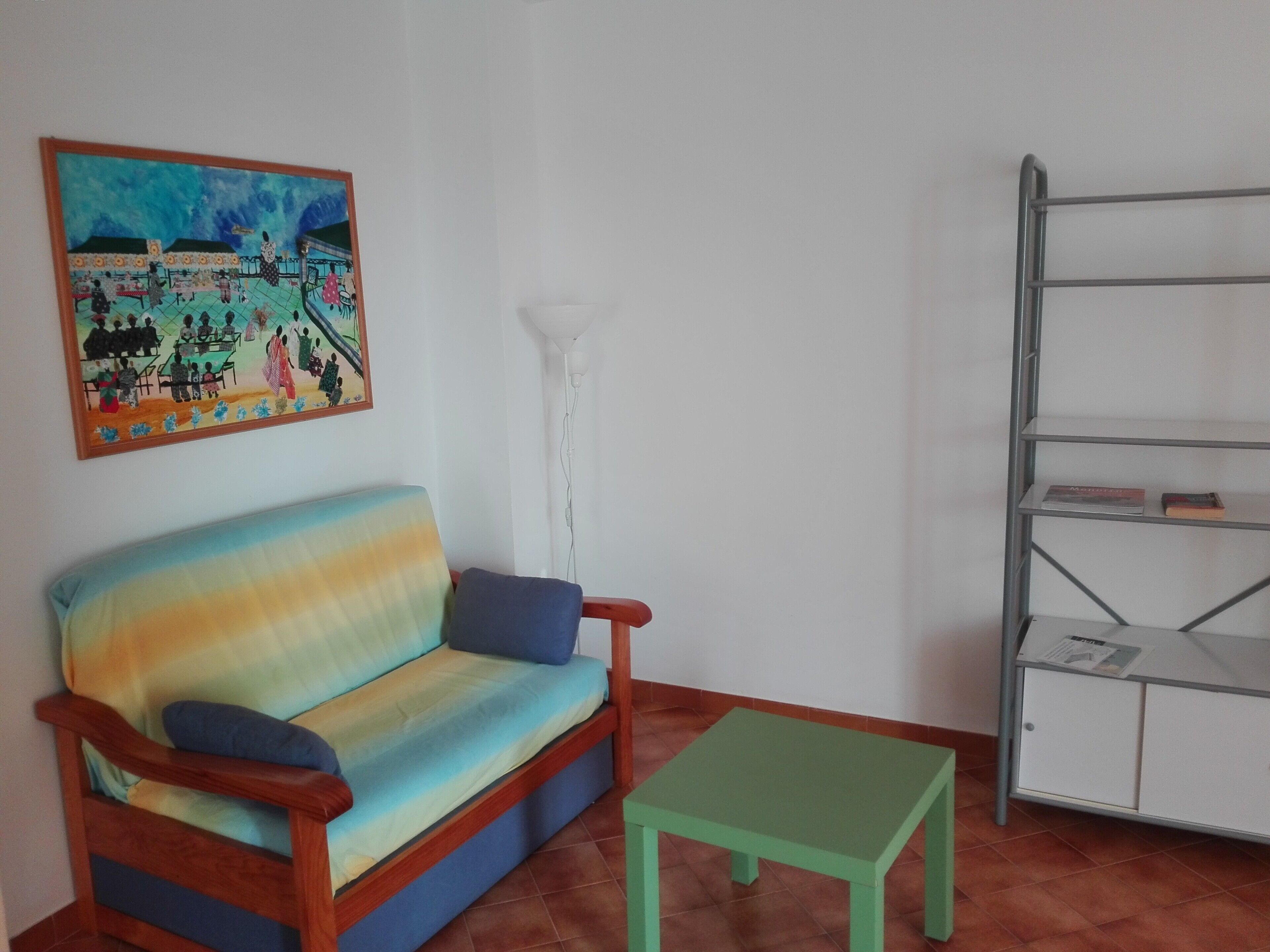 Una habitación con un sofá, una mesita, una estantería y un cuadro en la pared.