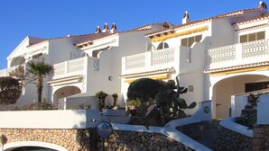 A white building with balconies, a stone wall, and a cactus. - Bouganville Apartment in Son Bou with Sea View (ALAIOR)