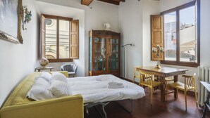 Ein Zimmer mit einem Bett, einem Esstisch mit Stühlen, einem Schrank mit Glastüren und einem großen Fenster.