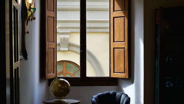 Ein Zimmer mit einem Globus auf einem kleinen Tisch, einem blauen Sessel und einem Fenster mit Holzjalousien.