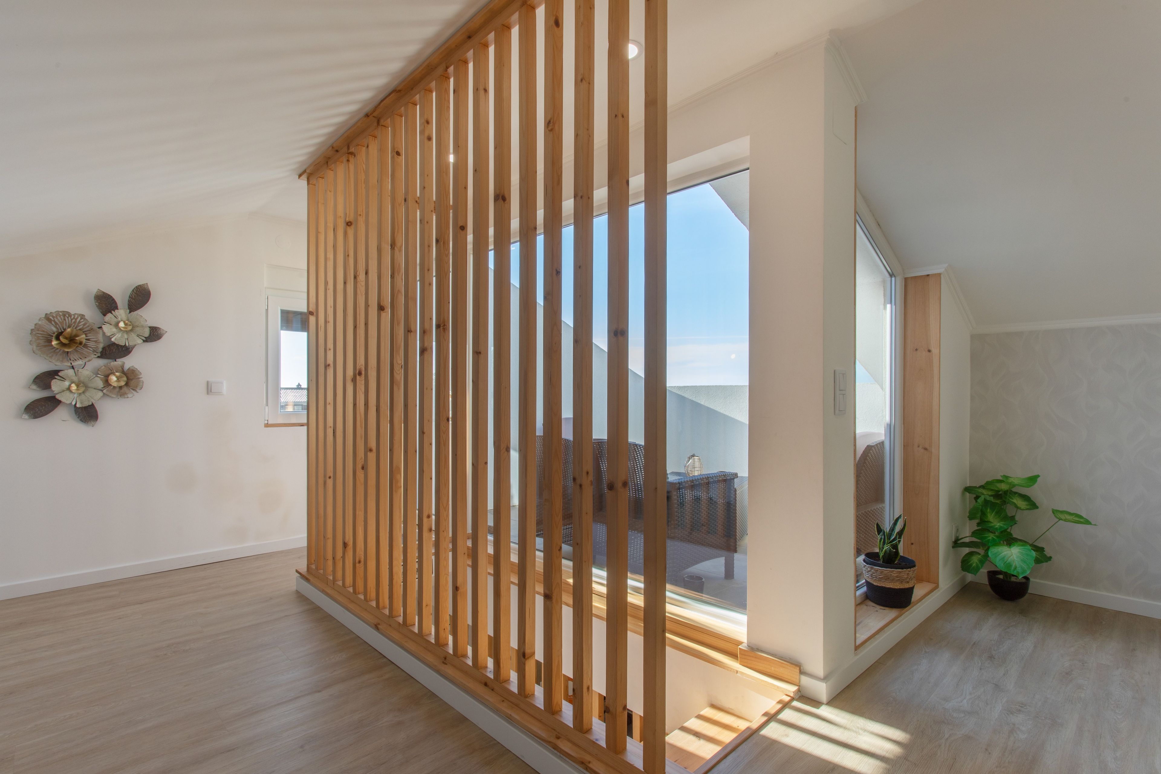 Een modern interieur met een houten roomdivider, een potplant en uitzicht door een glazen deur.
