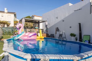 An outdoor swimming pool with inflatable toys, a covered seating area, and a white building in the background. - Holiday Home 'Refúgio das Barcas' with Sea View, Wi-Fi & Air Conditioning (Lourinha)