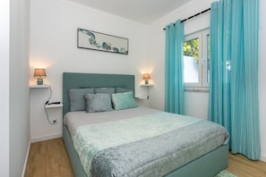 Une chambre à coucher avec un lit, deux lampes de chevet, une fenêtre avec des rideaux et une œuvre d’art accrochée au mur.