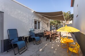 An outdoor patio with a table and chairs, a yellow umbrella, and a blue folding chair. - Holiday Home 'Refúgio das Barcas' with Sea View, Wi-Fi & Air Conditioning (Lourinha)