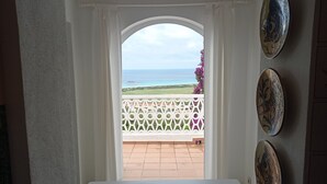 A room with a view of the ocean through an arched doorway, a white table, and decorative plates on the wall. - NiceView Apartment in Son Bou with Sea View – Ideal for Couples (ALAIOR)
