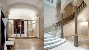Eine imposante Lobby mit Glastür, einer Marmortreppe und einer hohen Decke mit dekorativen Verzierungen.