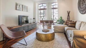 Ein modernes Wohnzimmer mit Fernseher, einem runden goldenen Couchtisch, einem braunen Sessel und einem beigen Sofa.