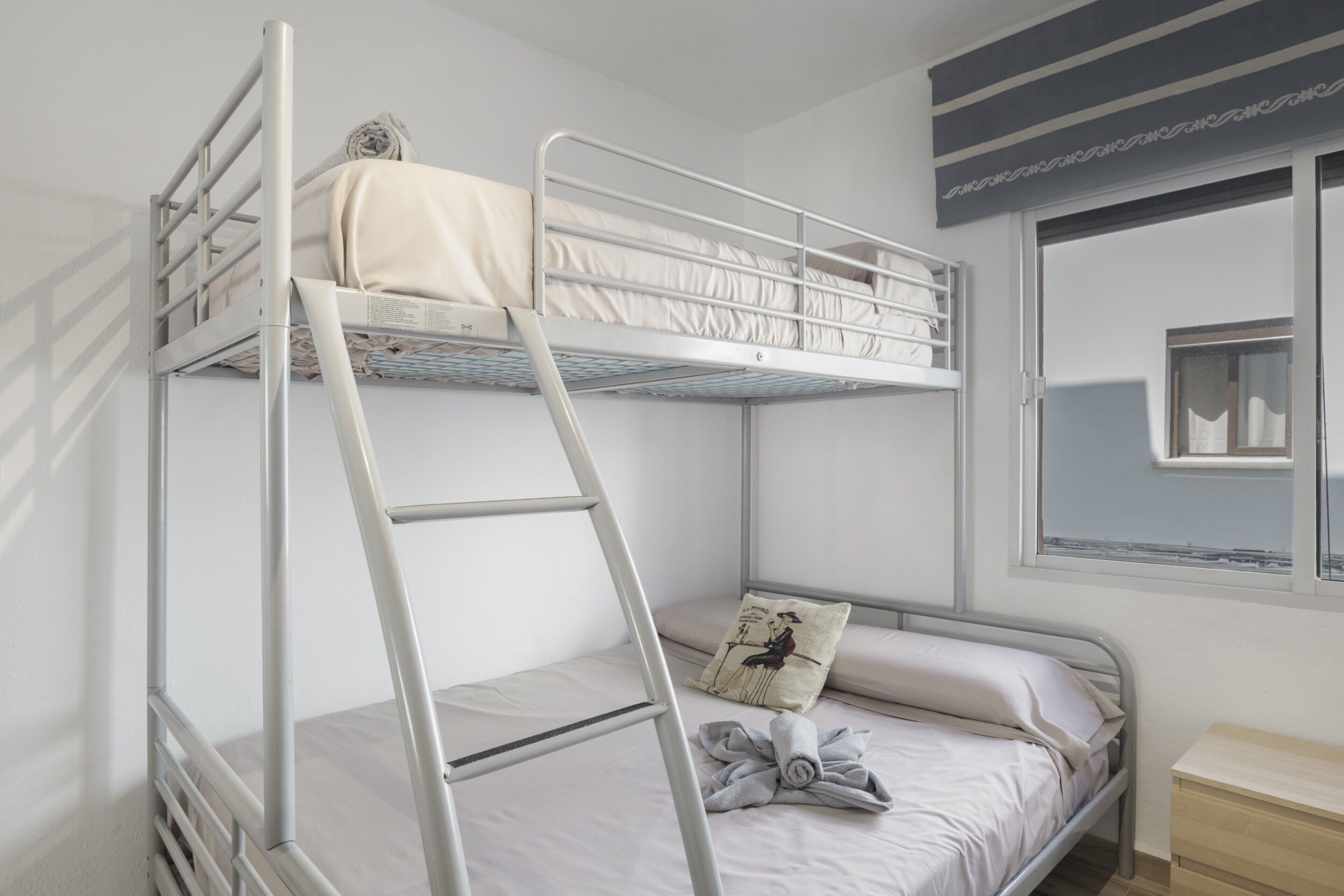 A bunk bed with a ladder, a bedside table, and a window with a view.