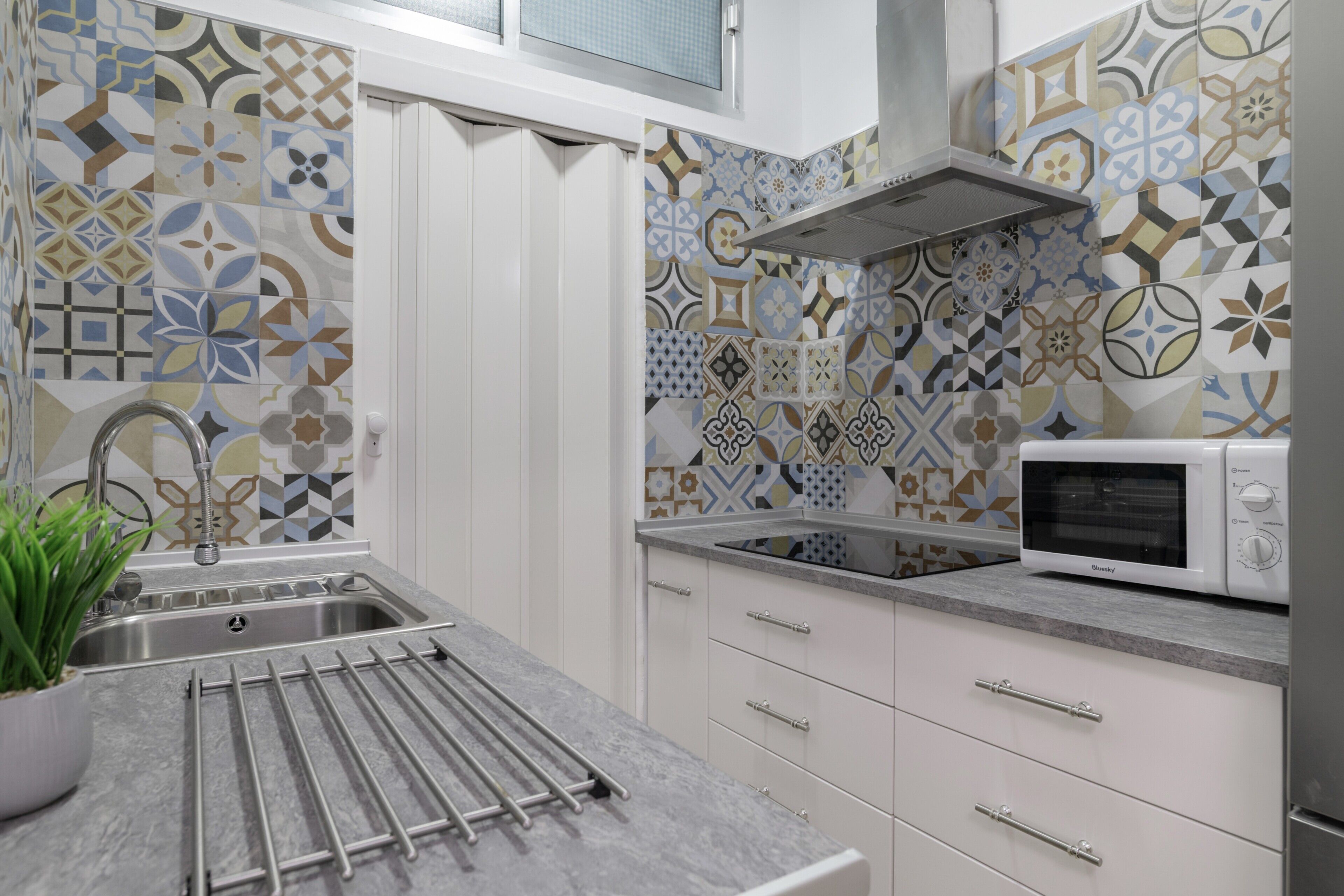 Una cocina con baldosas estampadas, un fregadero de acero inoxidable, un microondas y un tendedero.