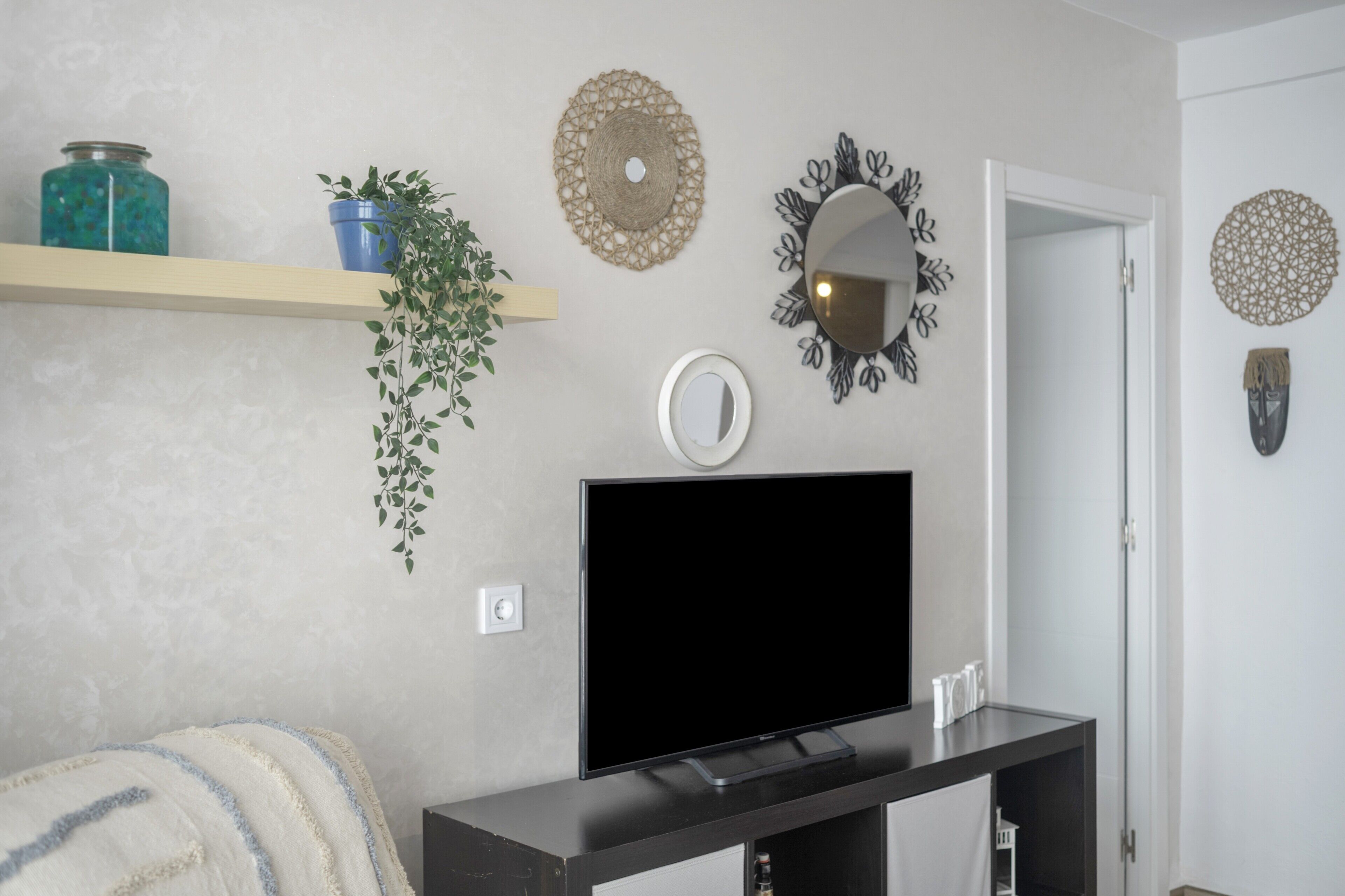 Een woonkamer met een flatscreen televisie, een plant, decoratieve wandversieringen en een plank met een pot en een bloempot.