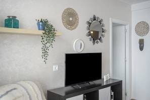 A living room with a flat-screen TV, a plant, decorative wall hangings, and a shelf with a jar and a potted plant. - 'Vista Mar Conil' Apartment with Sea Views, Shared Terrace and Wi-Fi (Conil de la Frontera)