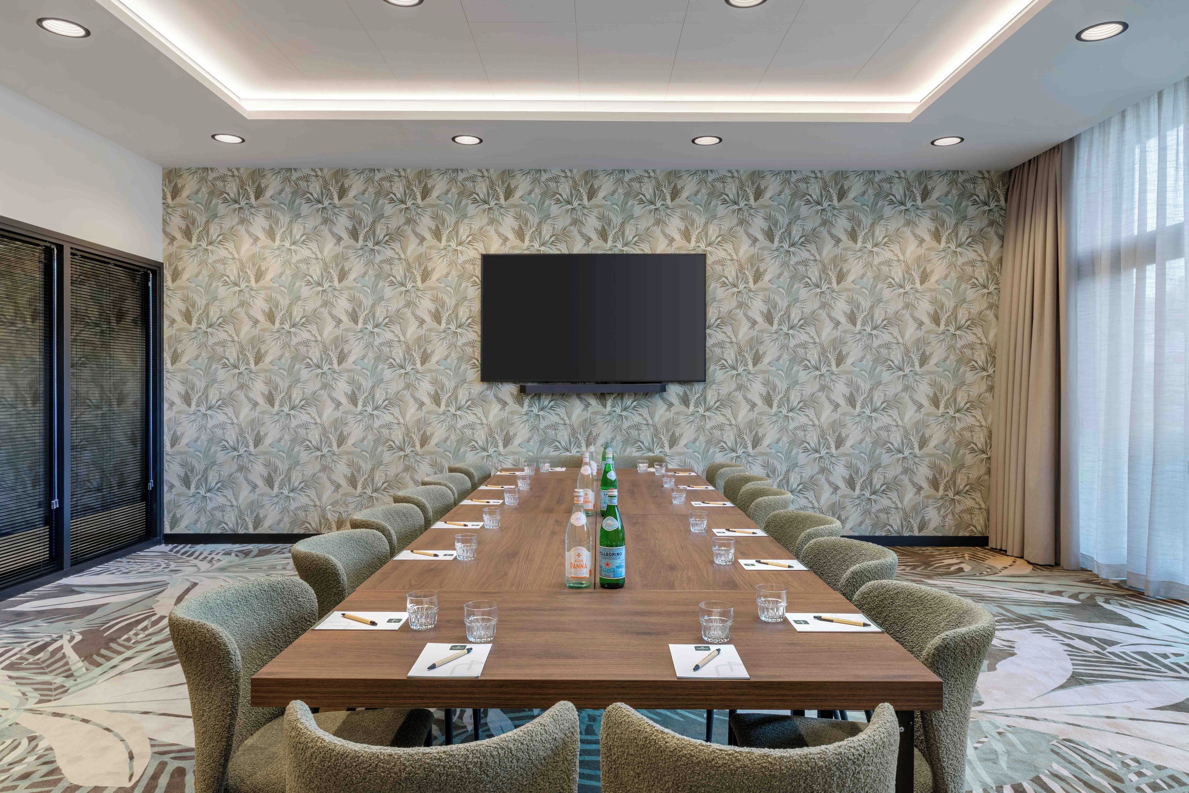 A conference room with a long table, chairs, a flat-screen TV, and a patterned wall.