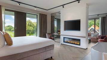 A modern bedroom with a large bed, a fireplace, a TV mounted on the wall, and a balcony with a view of the outdoors.