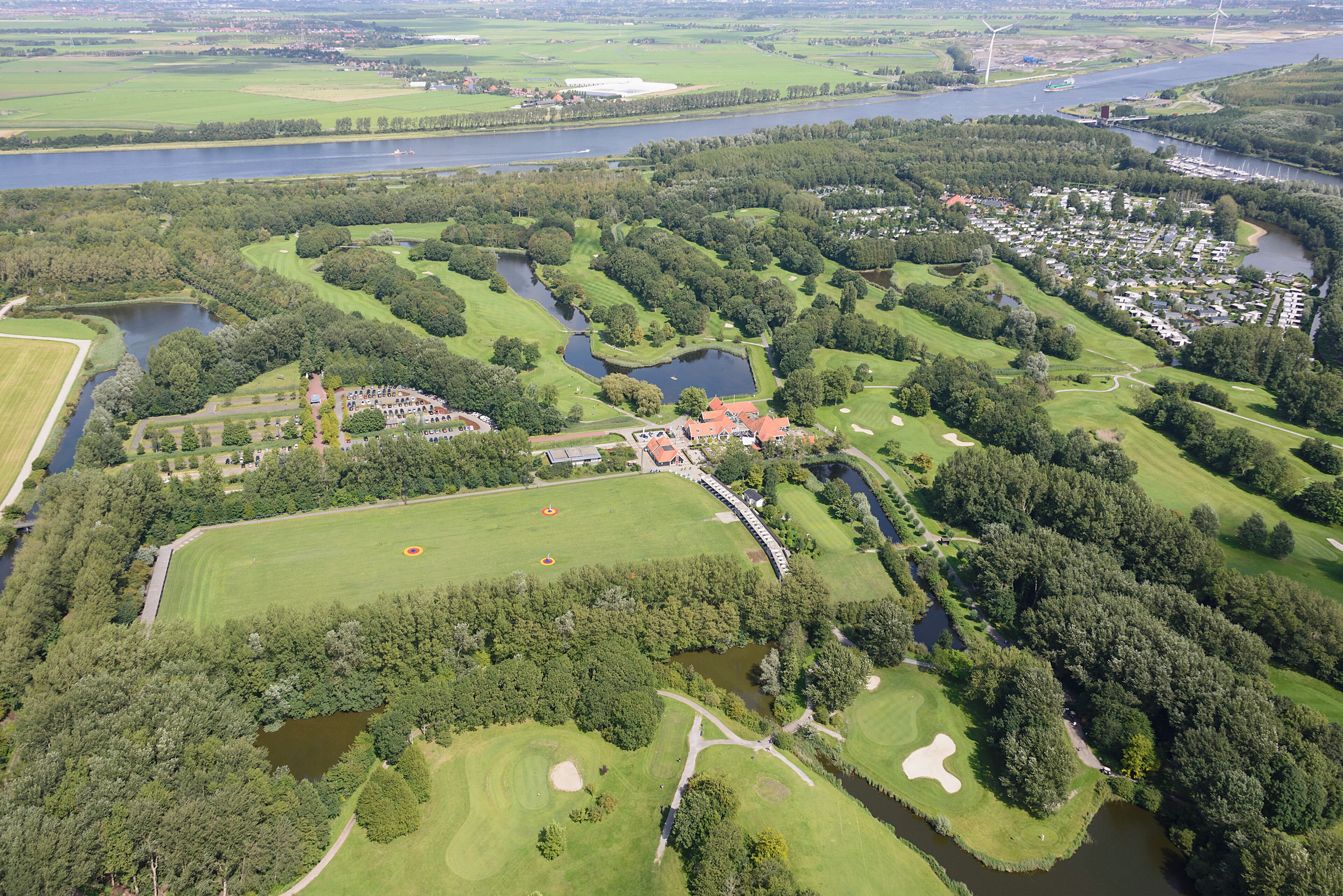 An aerial view of a golf course with multiple ponds, a residential area, and a river.