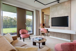 A modern living room with a flat-screen TV mounted on the wall, a sofa, a coffee table, and two chairs. - Spaarnwoude Park Hotel (Velsen-Zuid)