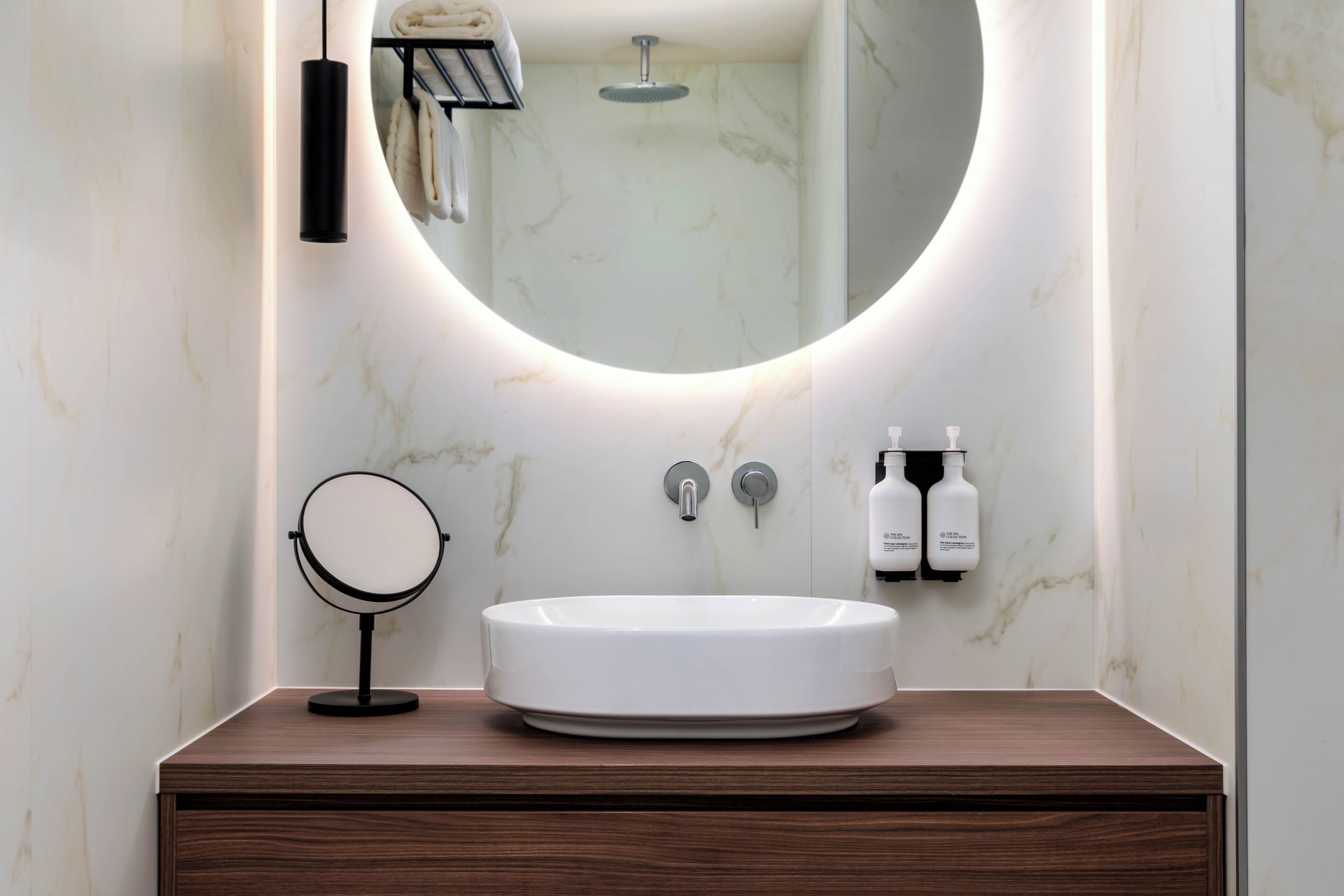 A bathroom with a round mirror, a white sink, and two bottles of shampoo on a wooden vanity.