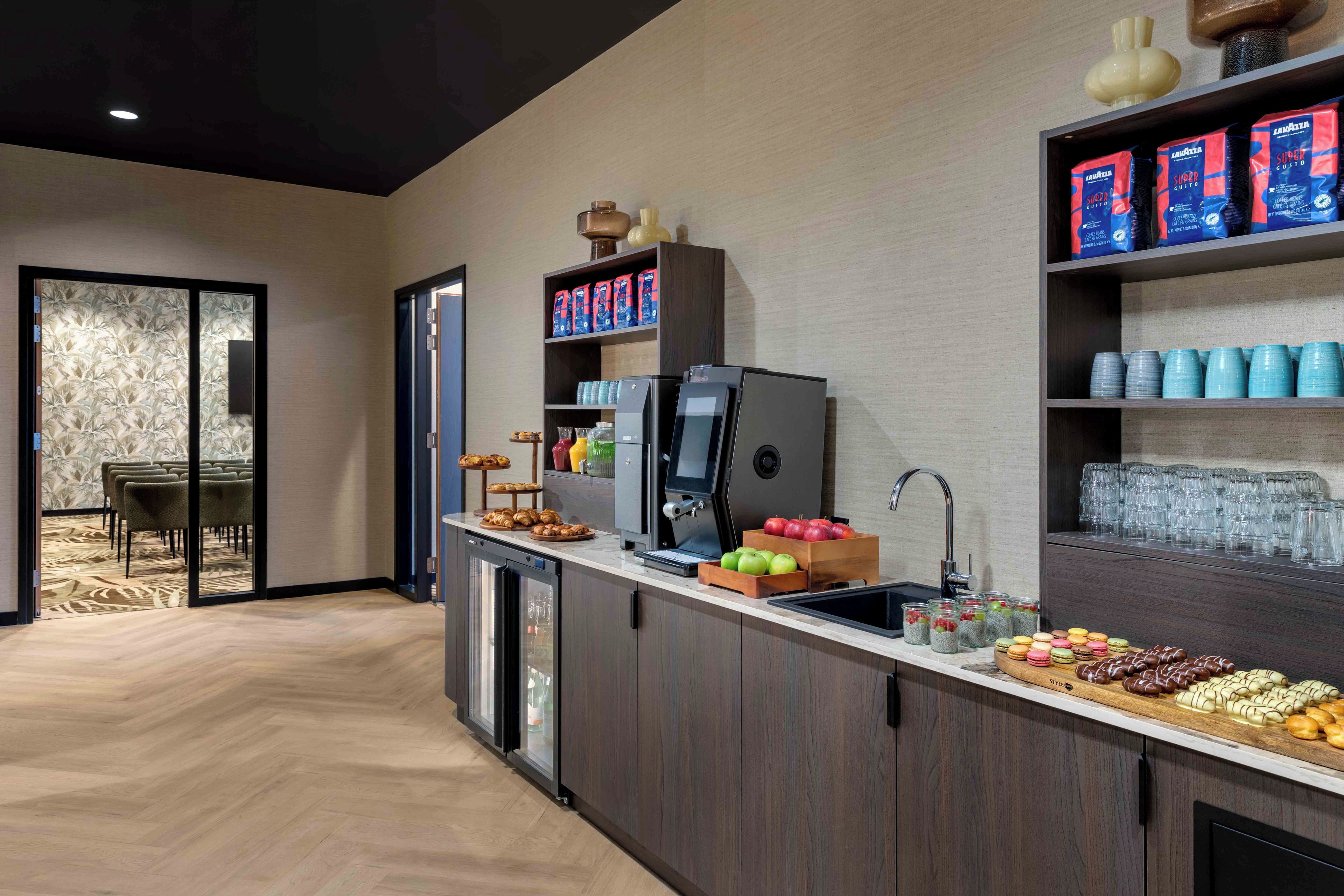 A modern kitchen area with a coffee station, a refrigerator, and a dining area with chairs.