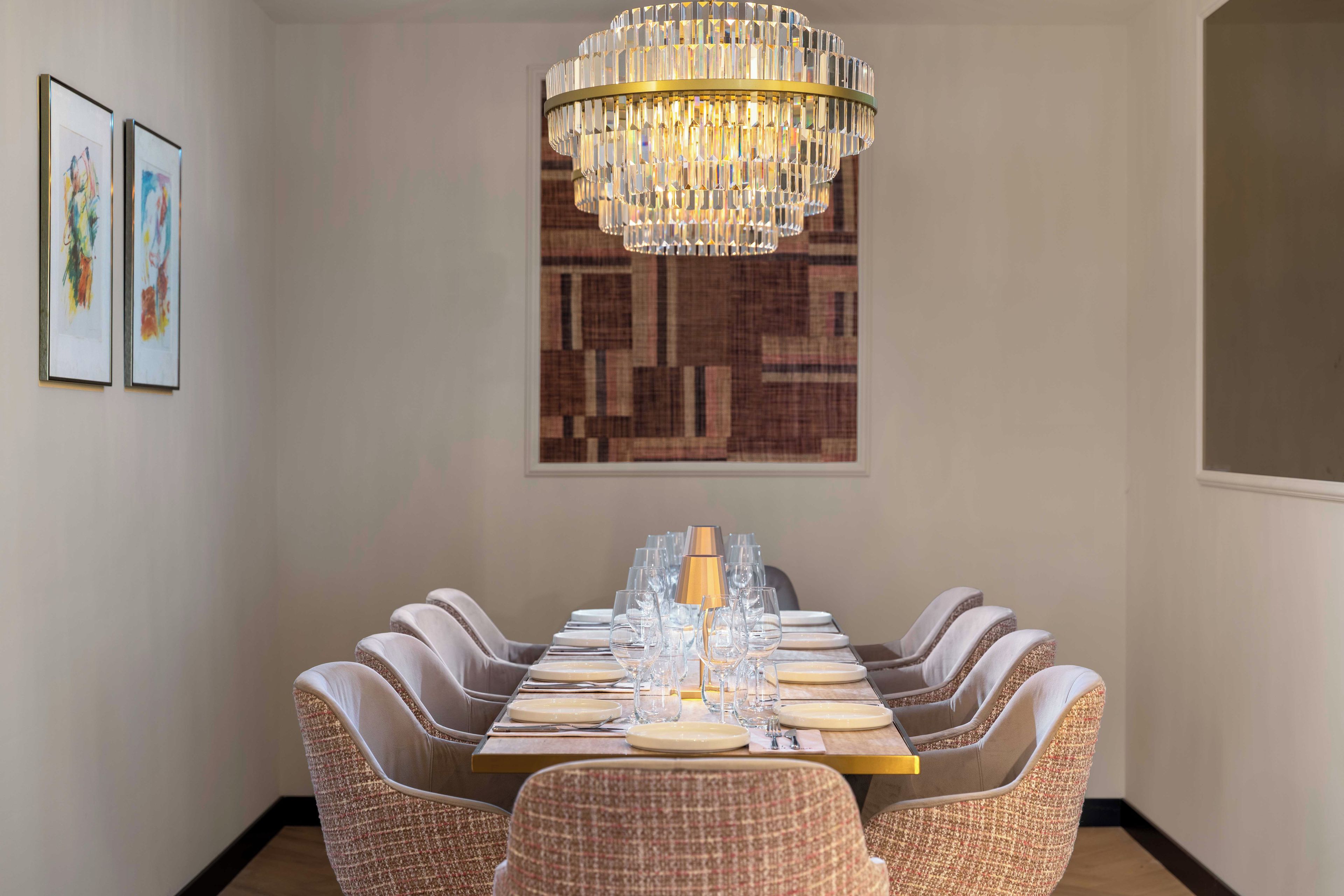 A dining area with a chandelier, a long table set for six, and two framed artworks on the wall.