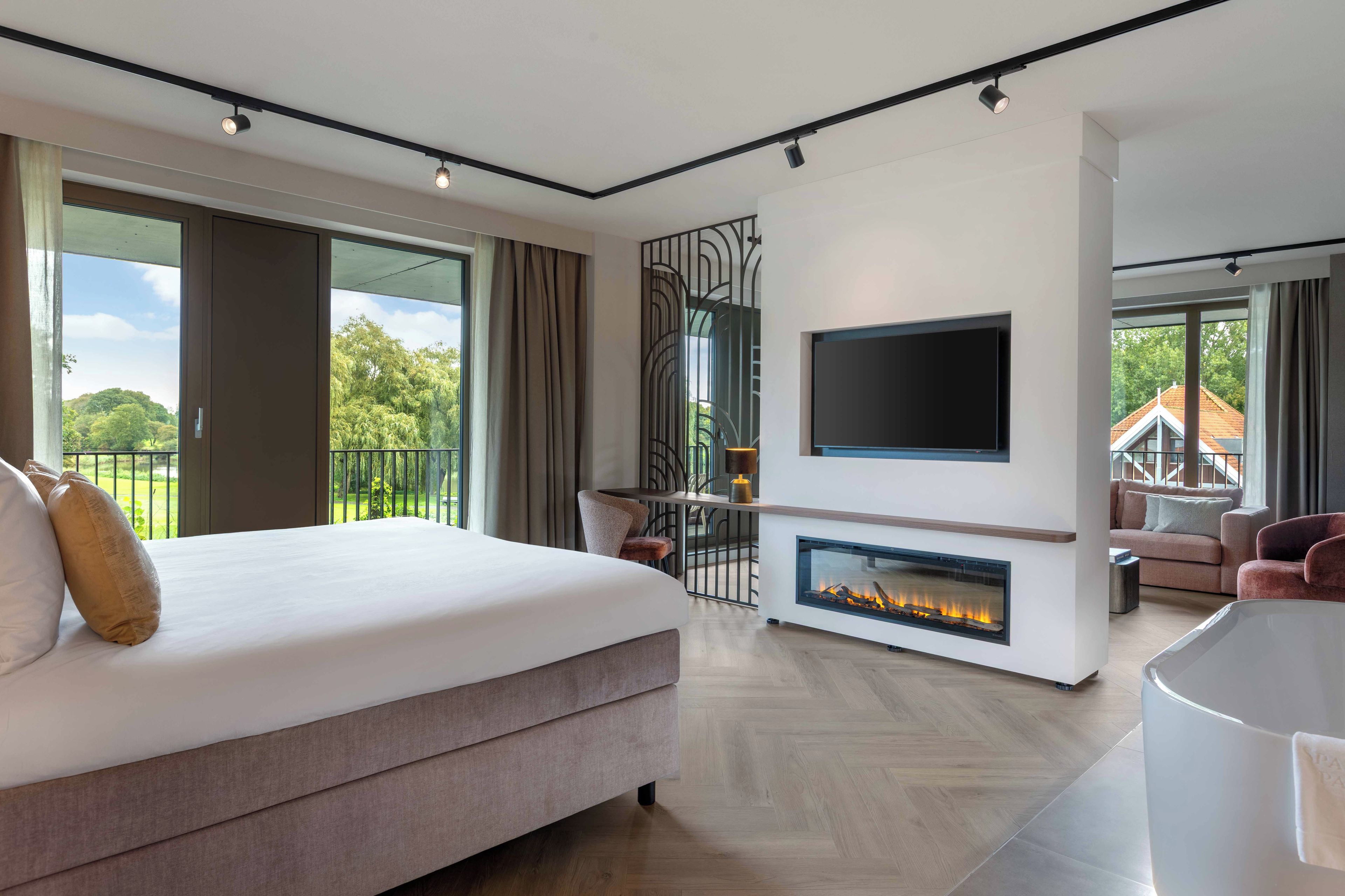 Une chambre moderne dotée d’un grand lit, d’une cheminée, d’un téléviseur fixé au mur et d’un balcon offrant une vue sur l’extérieur.