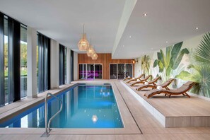 A modern indoor swimming pool with clear blue water, wooden loungers, and a tropical mural on the wall. - Spaarnwoude Park Hotel (Velsen-Zuid)