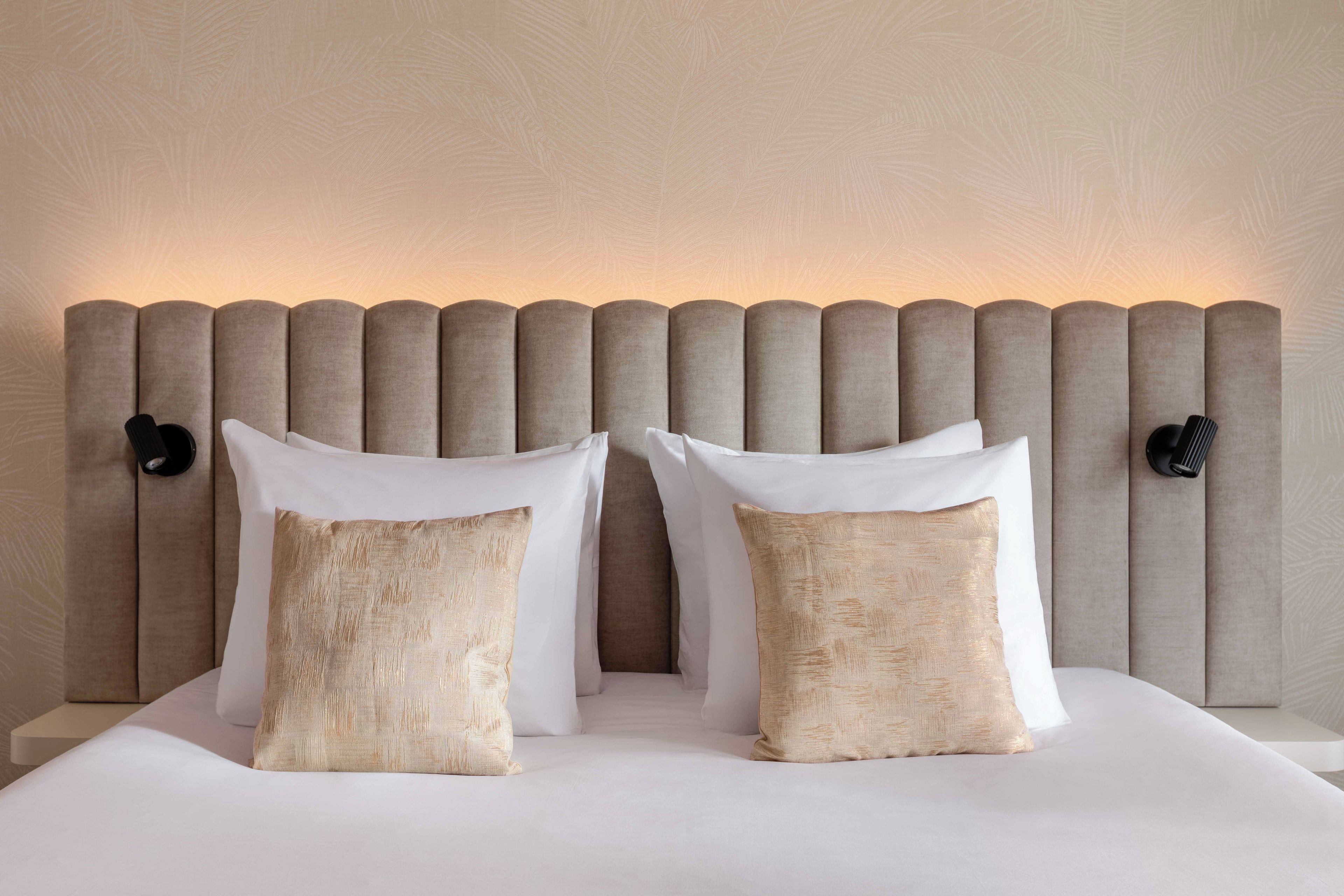 A bed with a headboard, two pillows, and two wall-mounted lamps.
