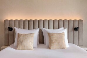 Una cama con cabecera, dos almohadas y dos lámparas fijadas a la pared.