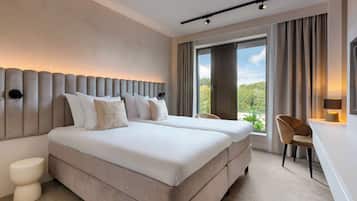 A hotel room with a large bed, a bedside table, a chair, and a window with a view of greenery.