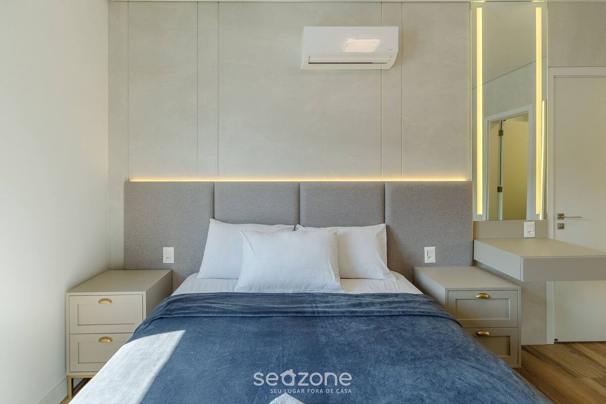 Une chambre à coucher moderne, comprenant un lit, des tables de chevet, une petite table et un climatiseur fixé au mur.
