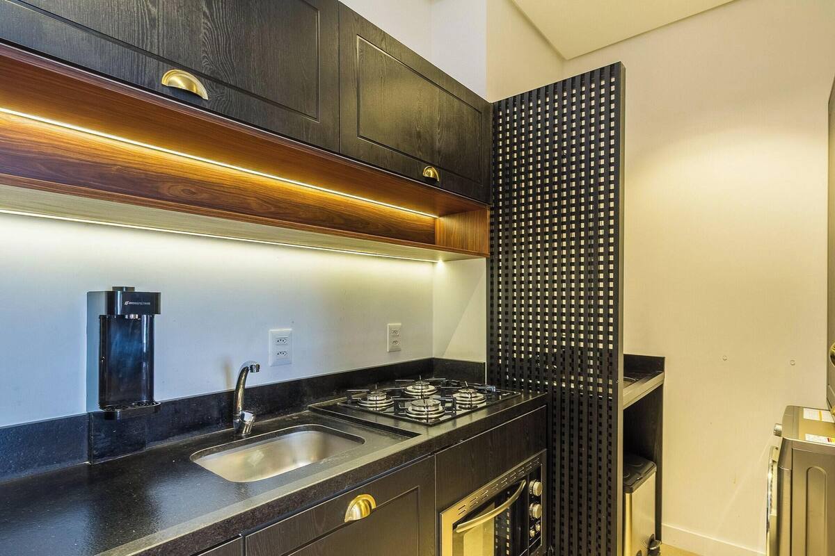 Une cuisine moderne avec des meubles en bois foncé, un évier en acier inoxydable, une cuisinière à gaz et un panneau perforé noir.