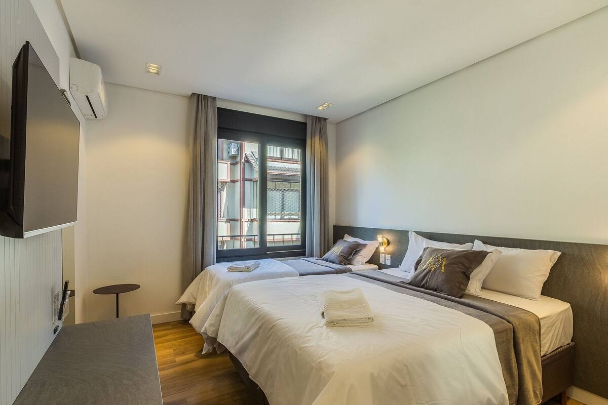 Une chambre d’hôtel avec deux lits, une télévision, une fenêtre avec des rideaux et une table de chevet.