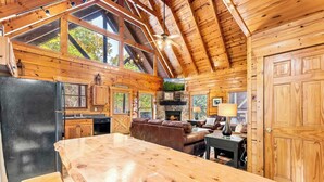 A spacious log cabin interior with a large wooden dining table, a cozy fireplace, and a stone fireplace. - 4BR Cabin for 8 w/ Game Room & Hot Tub Haven! (Sevierville)