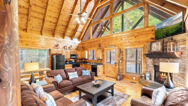 A spacious living room with a fireplace, wooden ceiling, and large windows. - 4BR Cabin for 8 w/ Game Room & Hot Tub Haven! (Sevierville)