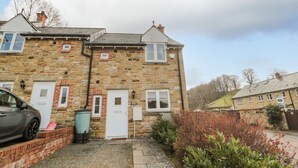 A stone building with a car parked in front, a door, and a small garden area. - Ramblers Cottage (Alnwick)