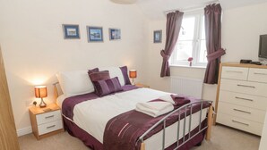 A bedroom with a bed, bedside tables, a dresser, a window with curtains, and framed pictures on the wall. - Ramblers Cottage (Alnwick)