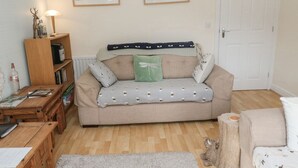 A cozy living room with a sofa, a wooden coffee table, a bookshelf, and a door. - Ramblers Cottage (Alnwick)
