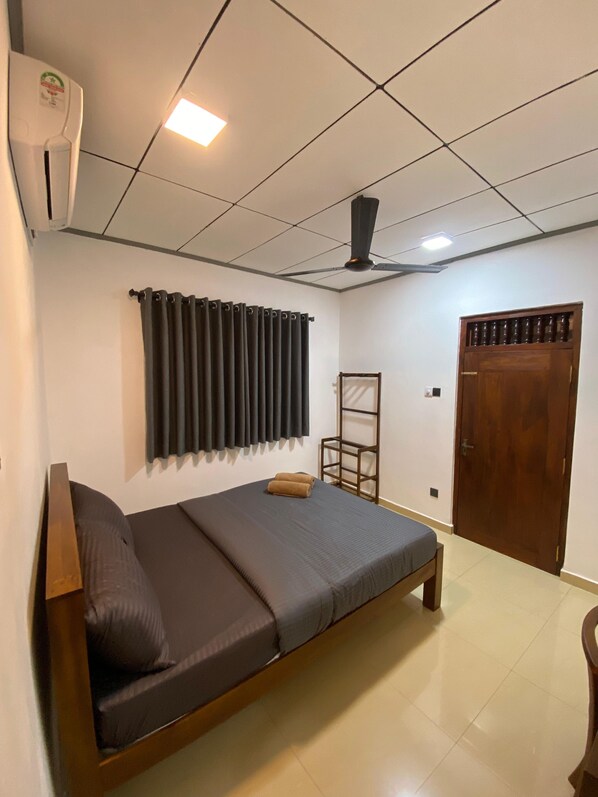 A bedroom with a bed, a ceiling fan, a window with curtains, a wooden door, and a radiator. - Sweden Villa Galle (Galle)