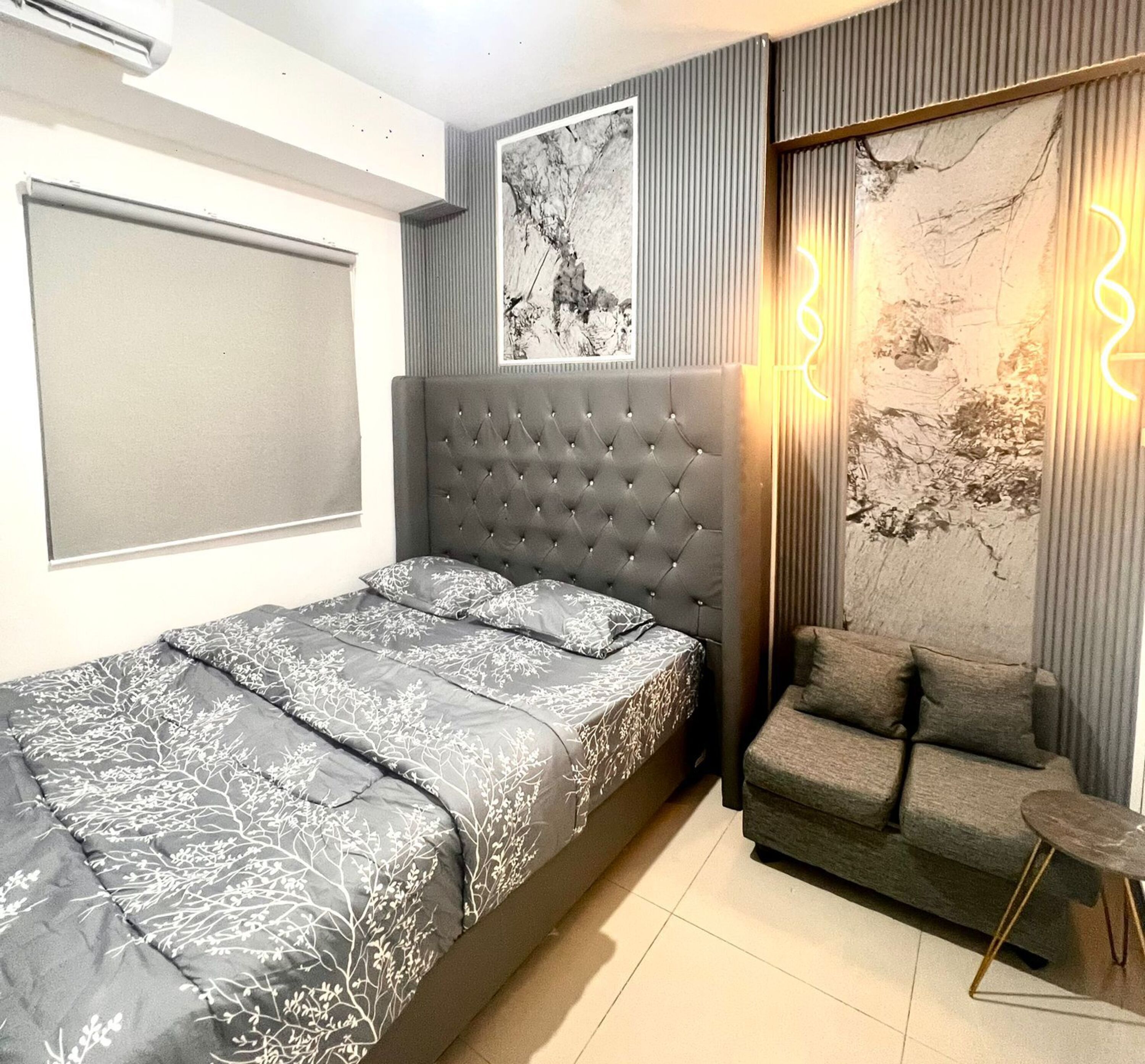 A bedroom with a bed, a sofa, a wall-mounted TV, and a framed artwork.