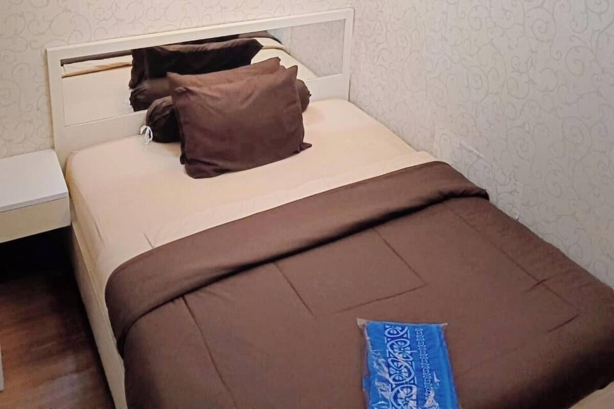 A neatly made bed with a headboard, a bedside table, and a wall clock.
