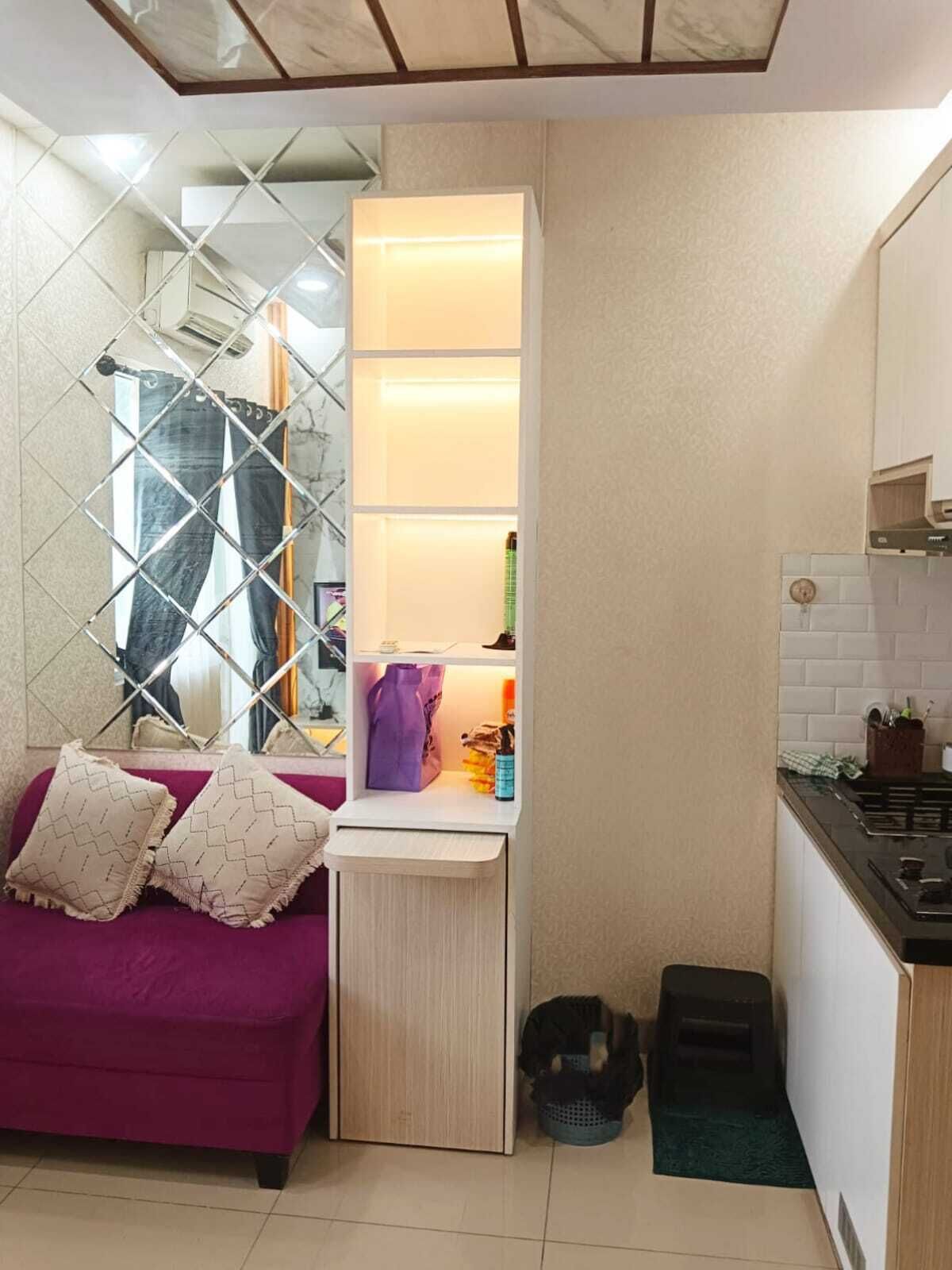 A compact living space with a kitchenette, a purple sofa with patterned cushions, a small storage unit with shelves, and a tiled floor.