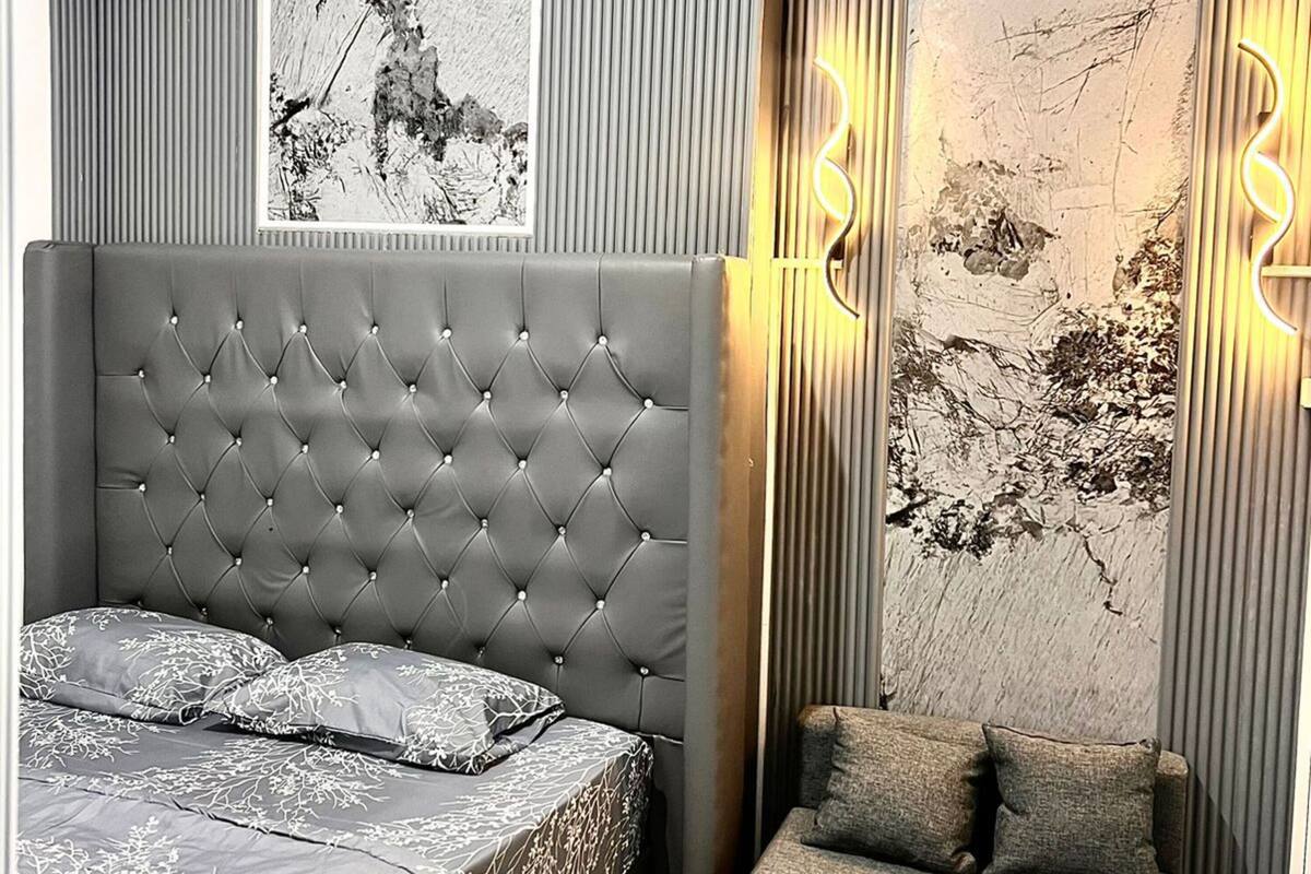A modern bedroom with a tufted headboard, a grey sofa, a small round table, and a large abstract painting on the wall.