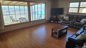 A spacious living room with a large window offering a scenic view, a leather sofa, a TV, and a small table.