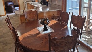 A dining area with a wooden table and chairs, a ceiling fan, and a kitchen in the background.