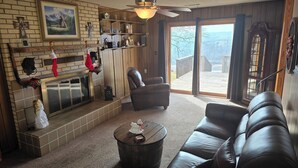 A cozy living room with a fireplace, leather furniture, and a large window offering a view of the outdoors.