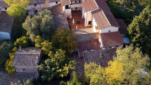 A traditional villa with multiple terracotta-tiled roofs, surrounded by lush greenery and trees. - Relais de Ricci (Impruneta)