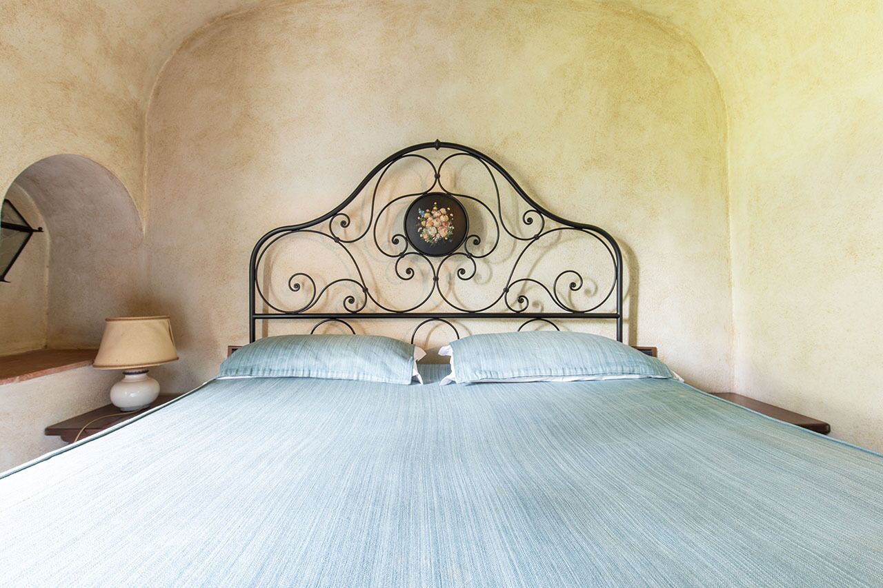 Ein Bett mit Metallkopfteil, einer Lampe und einer Wand mit einem Rundbogenfenster.