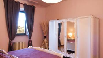 A bedroom with a bed, a wardrobe, a radiator, and a window with curtains.