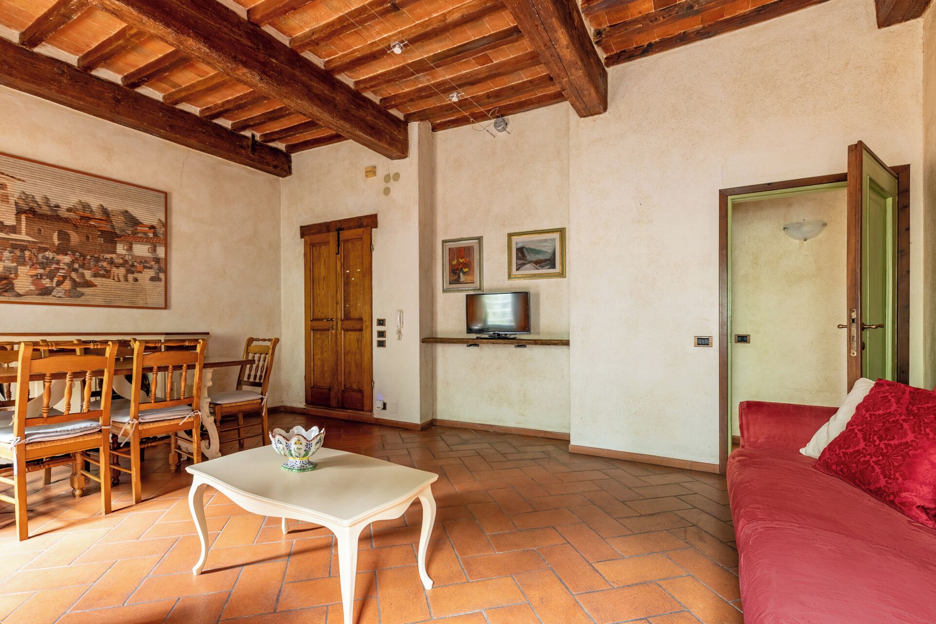 A living room with a wooden table, chairs, a red sofa, a television, and a door.